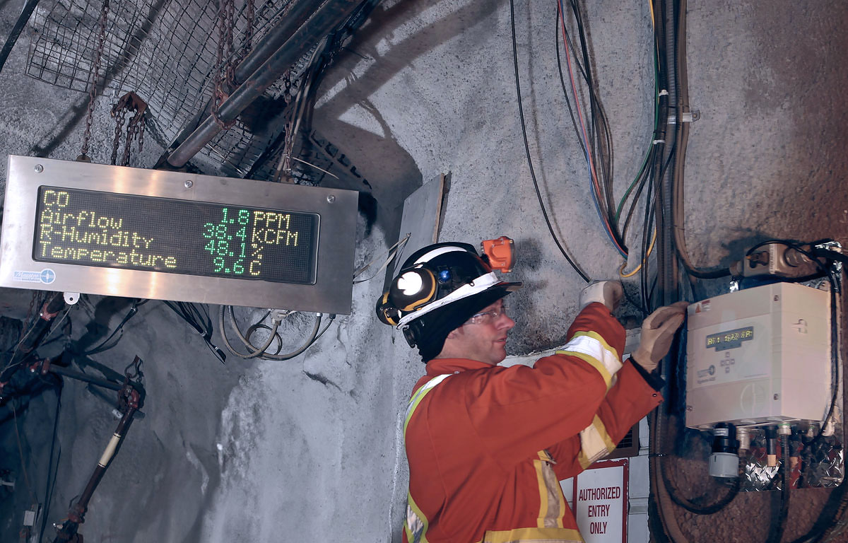 Image of an underground miner working on a Vigilante AQS system. Behind him is a Superbrite Marquee Display mounted from the tunnel ceiling.